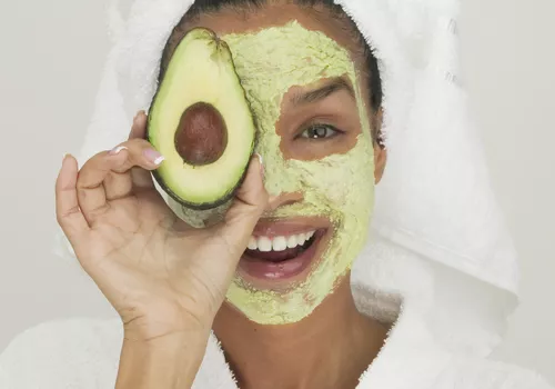Portrait of a young woman wearing a facial mask holding a slice of avocado