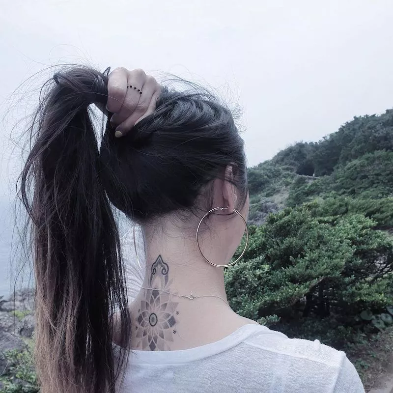 Woman lifts hair to reveal intricate mandala tattoo on back of neck