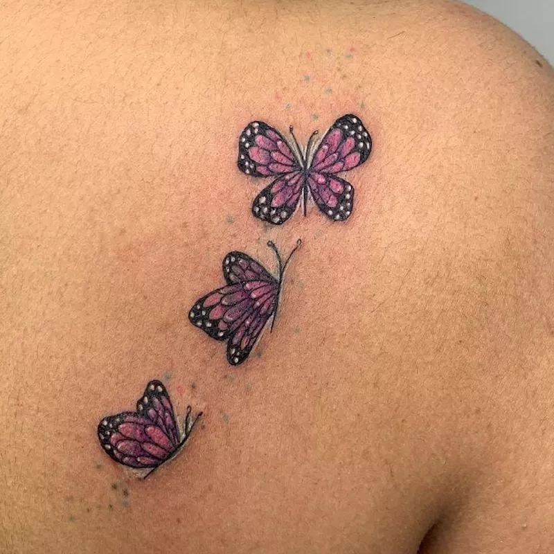 Set of three pink butterfly tattoos on back of shoulder