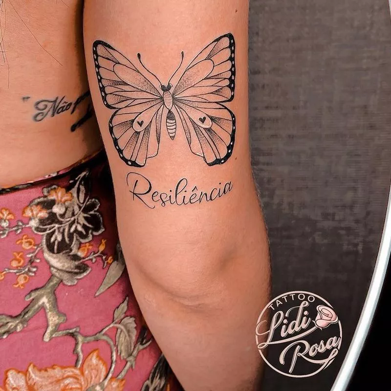Arm tattoo with butterfly and phrase "Resiliencia"