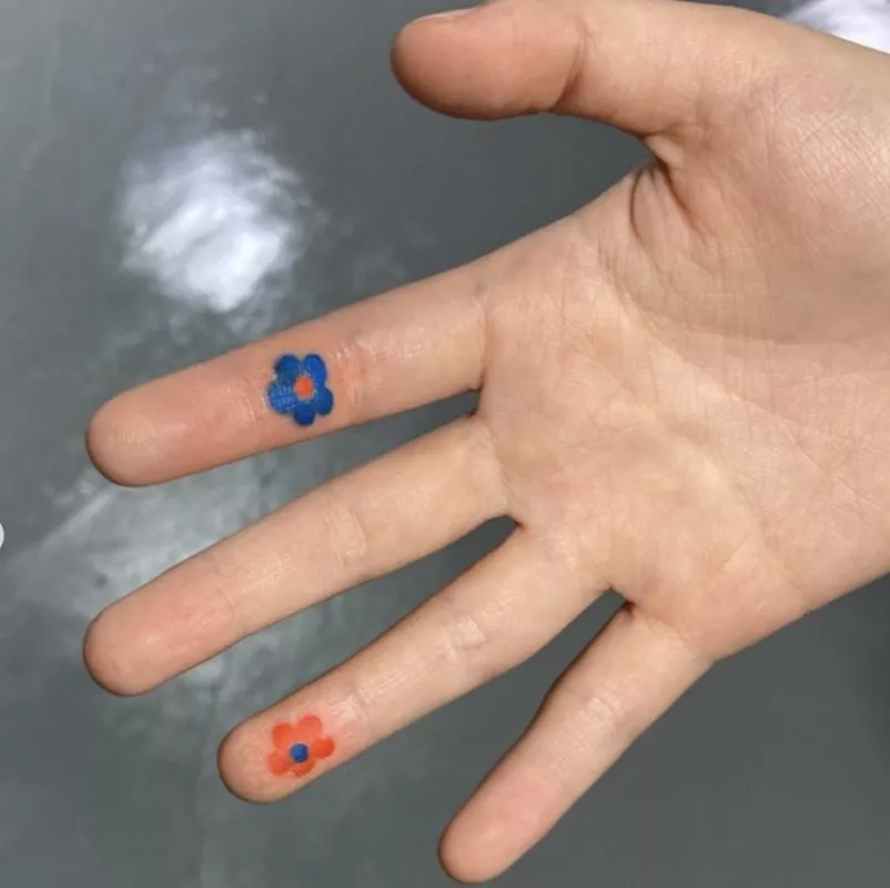 Blue and orange small flower tattoos on inner fingers