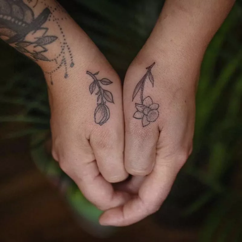 Two different flower tattoos on side of thumbs