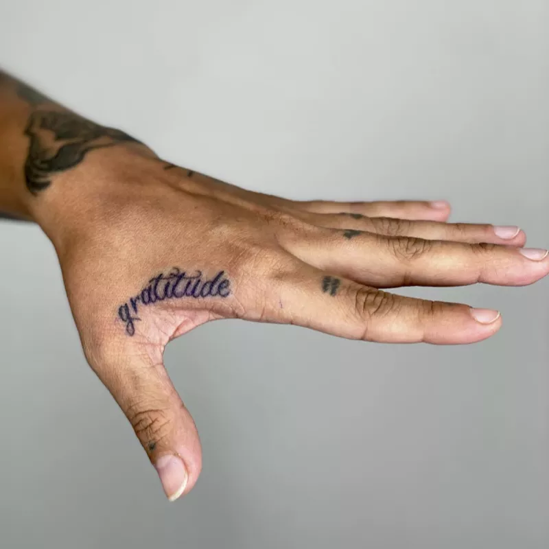"Gratitude" word tattoo on hand webbing