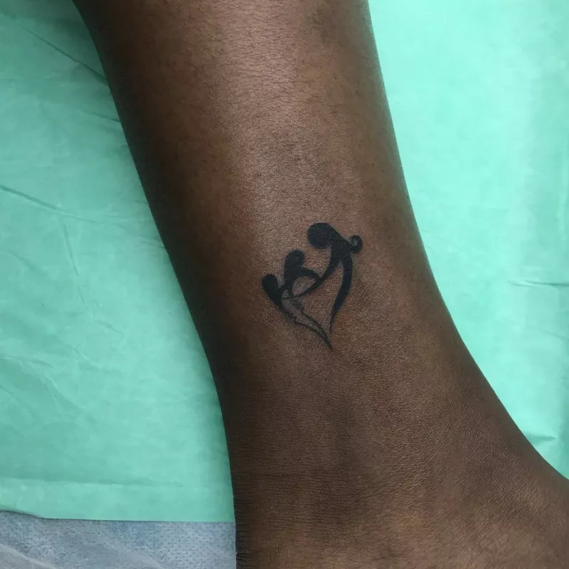 Small ankle tattoo of figures holding hands in heart shape
