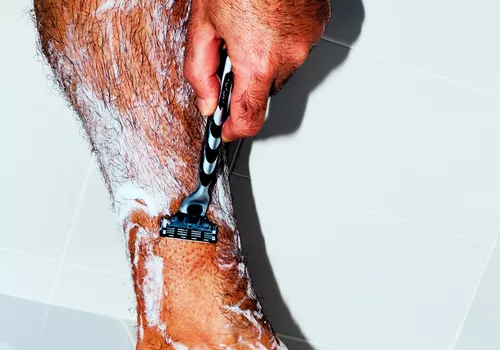 Man shaving his leg in the shower.