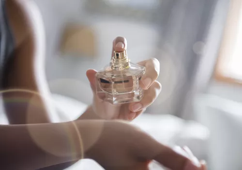woman spritzing perfume in a white bedroom