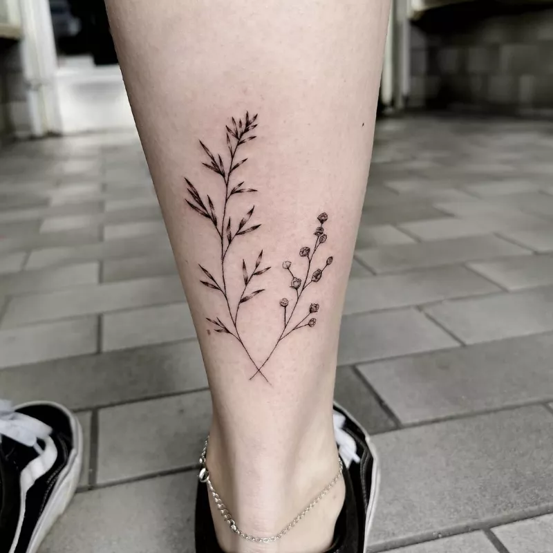 lower calf tattoo of branches with negative space leaves and blooms