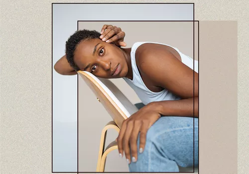 BIPOC Portrait Sitting Down Against a Chair with a Long Buzzcut Style Haircut Against Abstract Background