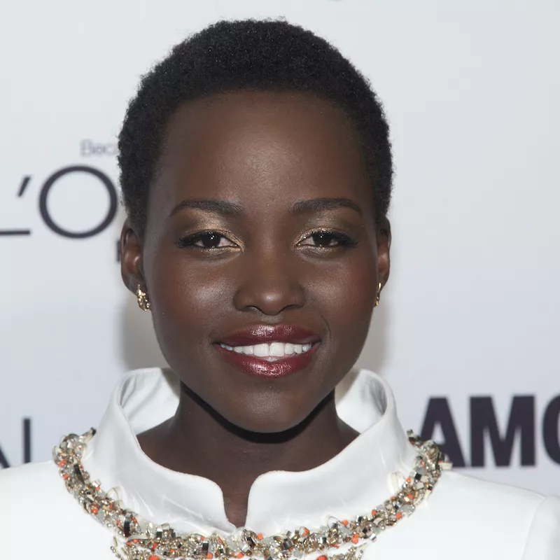 Lupita Nyong'o wears a short Afro hairstyle and warm-toned makeup