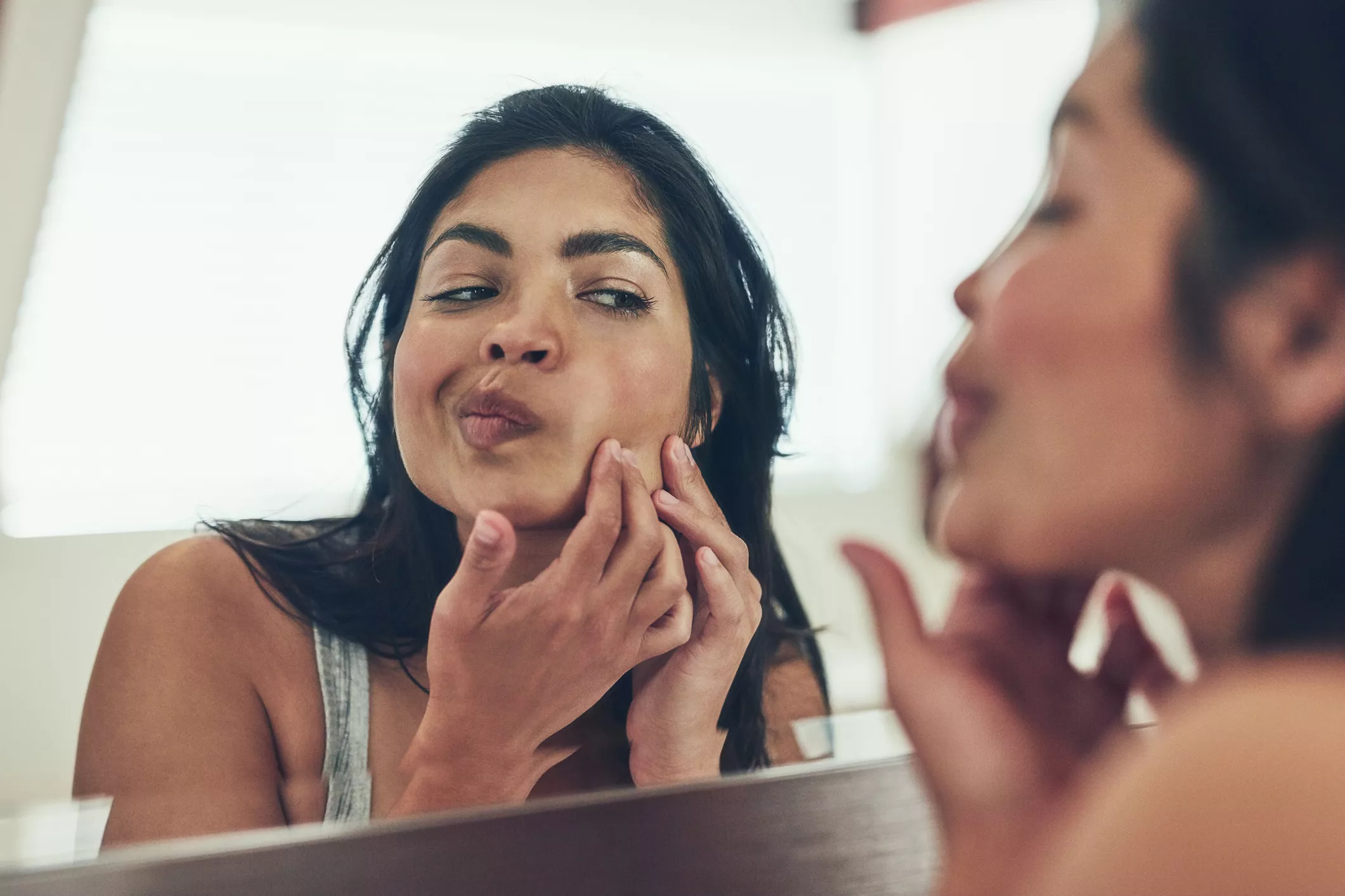 Woman popping pimple in mirror.