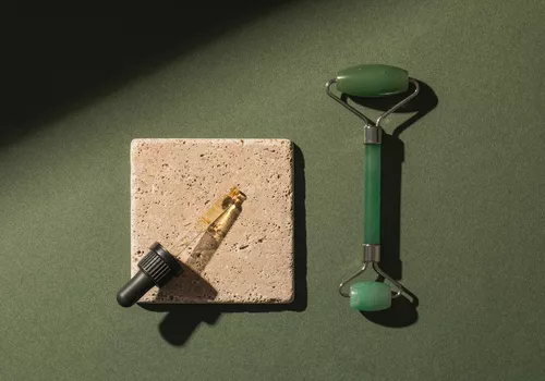 Eye serum in a dropper and a jade roller on a green background