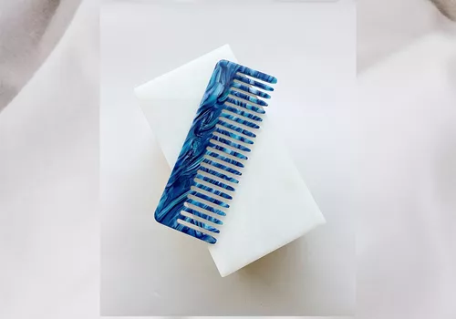 A beautiful blue wide-tooth comb on a white background.