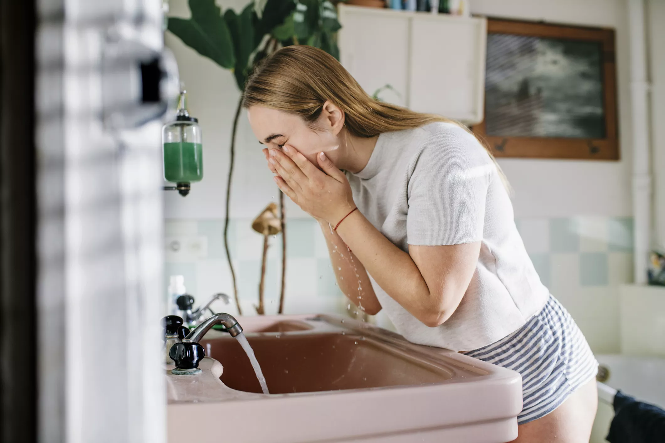 woman washing face at pink sink