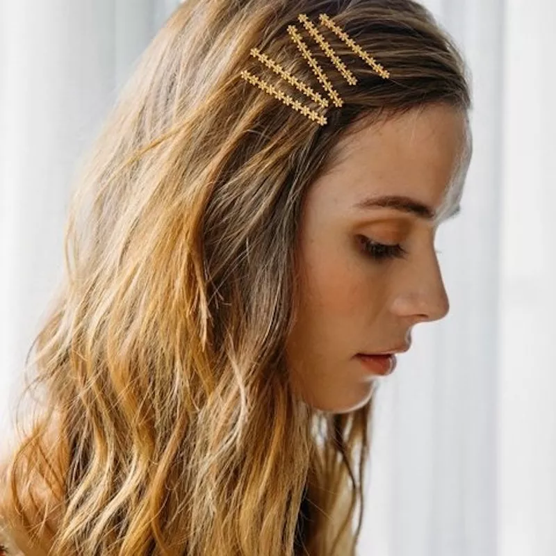 Woman with wavy dirty blonde hair and intricate daisy gold bobby pin stack
