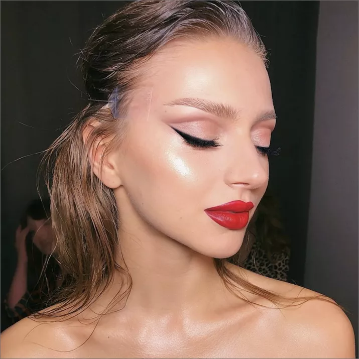 Woman with pink cut-crease eyeshadow, winged liner, red lip, and highlighter
