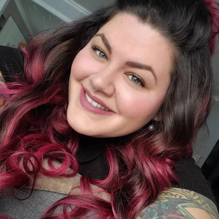 Woman wears long, curled pink ombre hair with dark roots