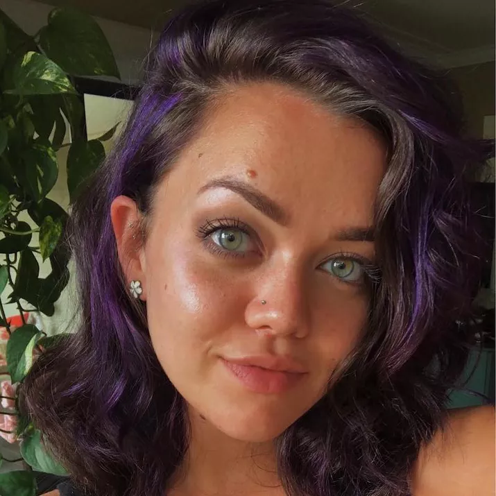 Woman with tousled shoulder-length hair and subtle purple highlights