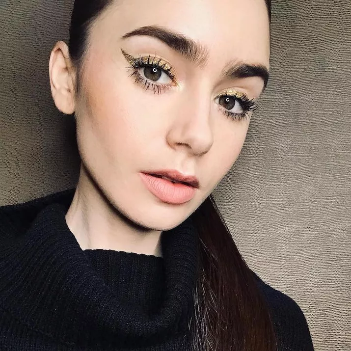 Lily Collins wears gold winged eyeliner, long lashes, and her signature strong eyebrows