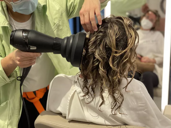 A hairstylist begins diffusing hair on a client.