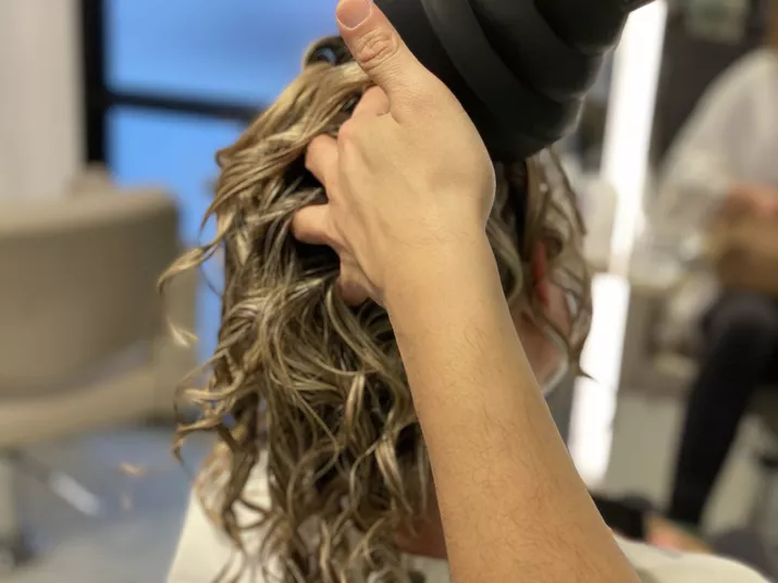 A hairstylist starts building volume while diffusing a client's hair. 
