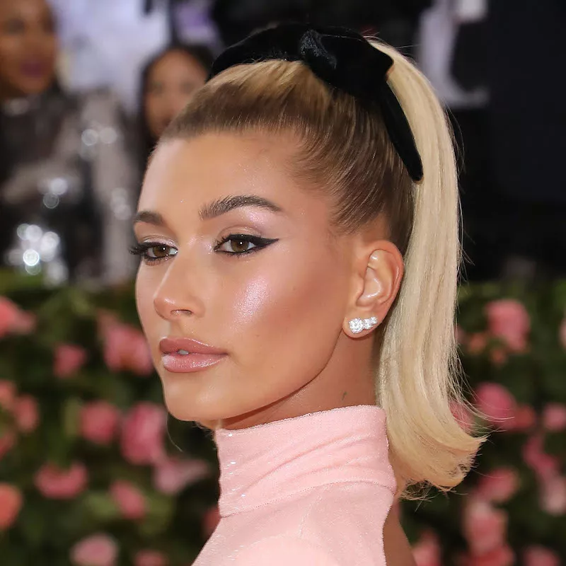 Hailey Bieber wears a high ponytail hairstyle with an oversized black bow