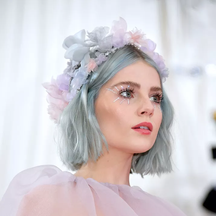 Lucy Boynton wears a pastel blue bob with bedazzled eye makeup and a flower crown
