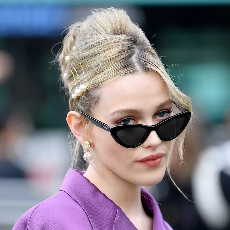 Victoria Pedretti wears a teased bouffant updo with pearl bobby pins and cat-eye sunglasses