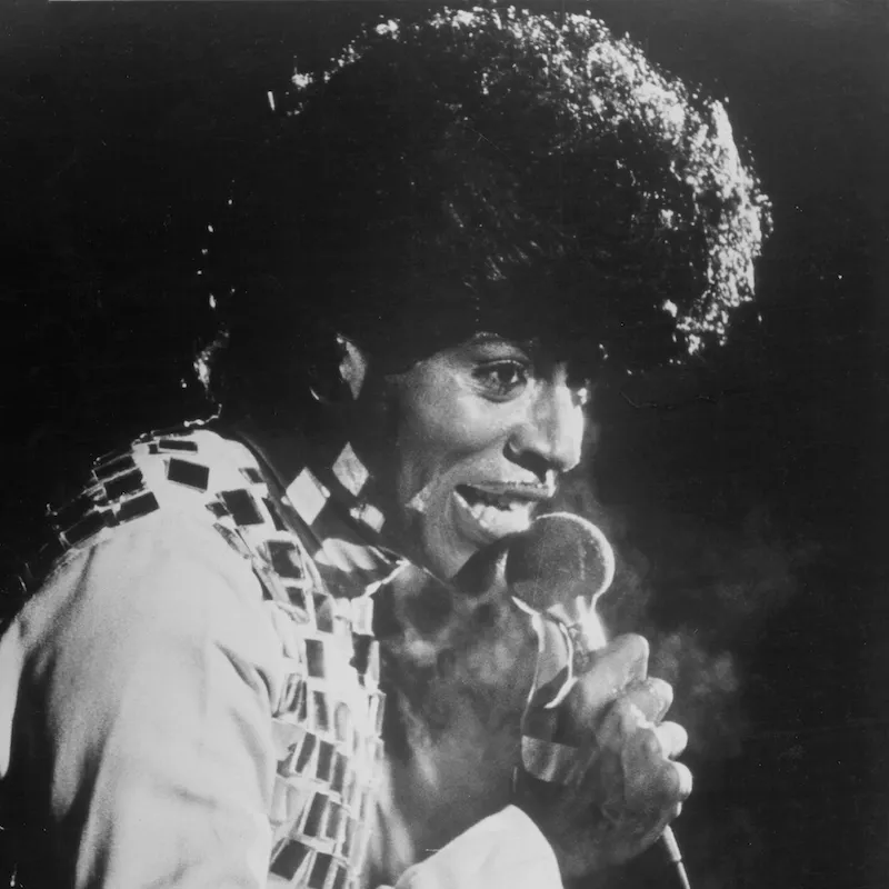 Little Richard wears a curly bouffant hairstyle while performing