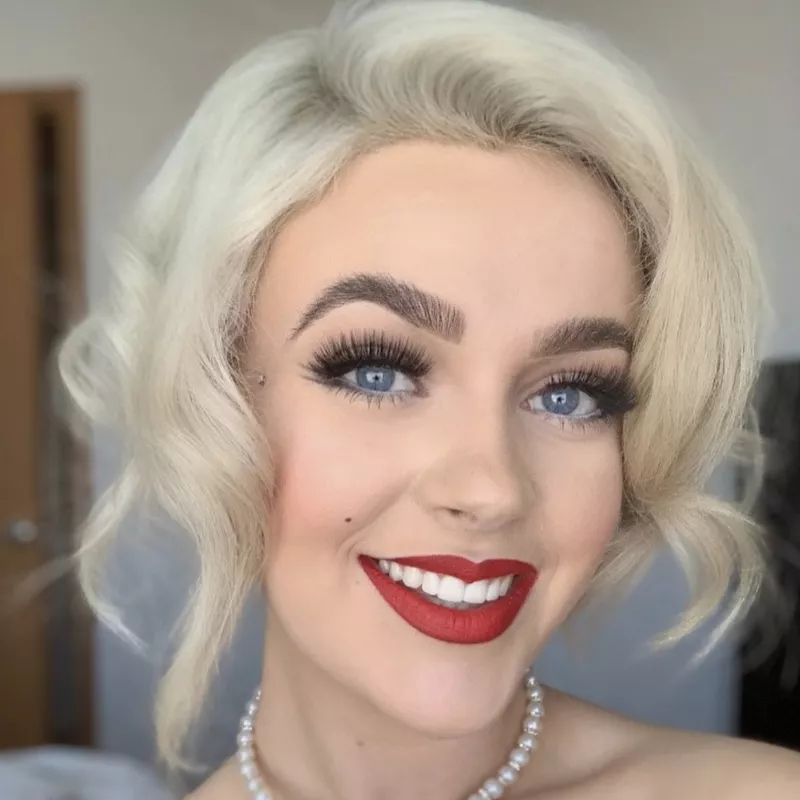 Marilyn Monroe hair and makeup featuring curled platinum bob, red lips, and lashes