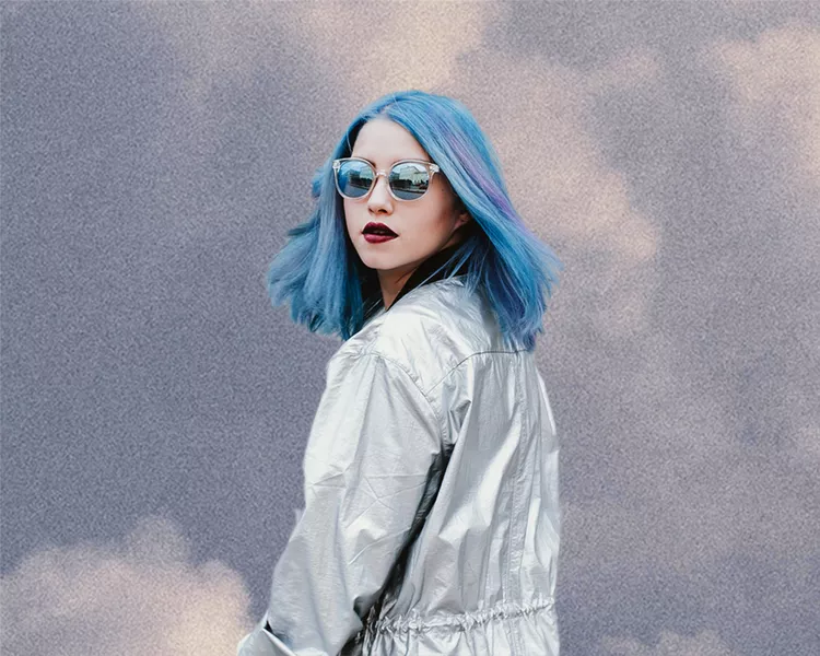 woman with blue hair looking backward with cloud background