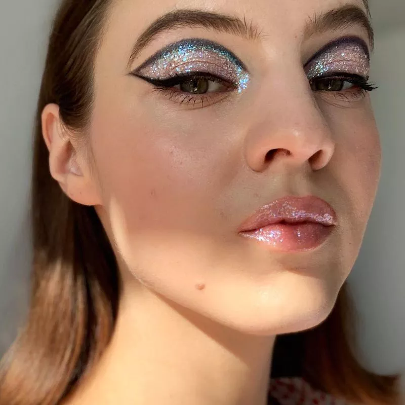 Woman wears holographic glitter eyeshadow with black graphic cut crease
