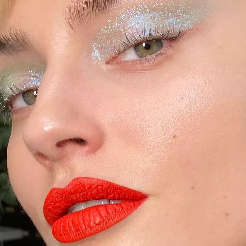 Model with iridescent glitter eyeshadow and red-orange lipstick