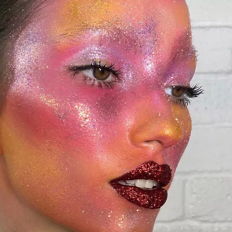 Model with full face of pink, orange, and yellow glitter with red glitter lip