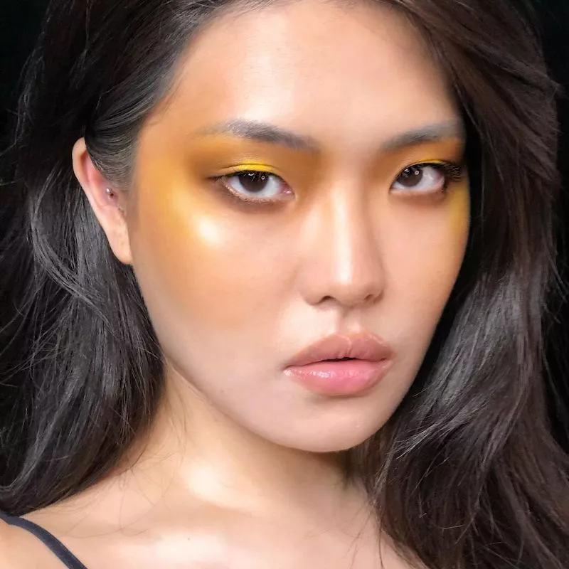 Model wears a glowy makeup look featuring yellow eyeshadow