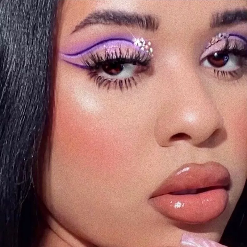 Makeup artist wears purple cut crease eyeliner with silver glitter and neutral lip gloss