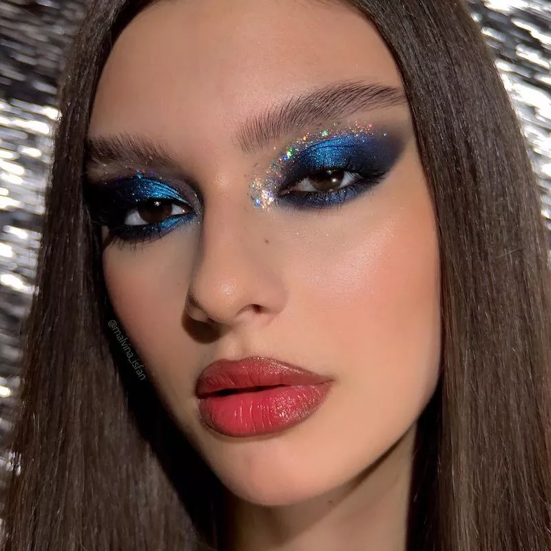 Model wears deep blue eyeshadow with silver glitter cut crease
