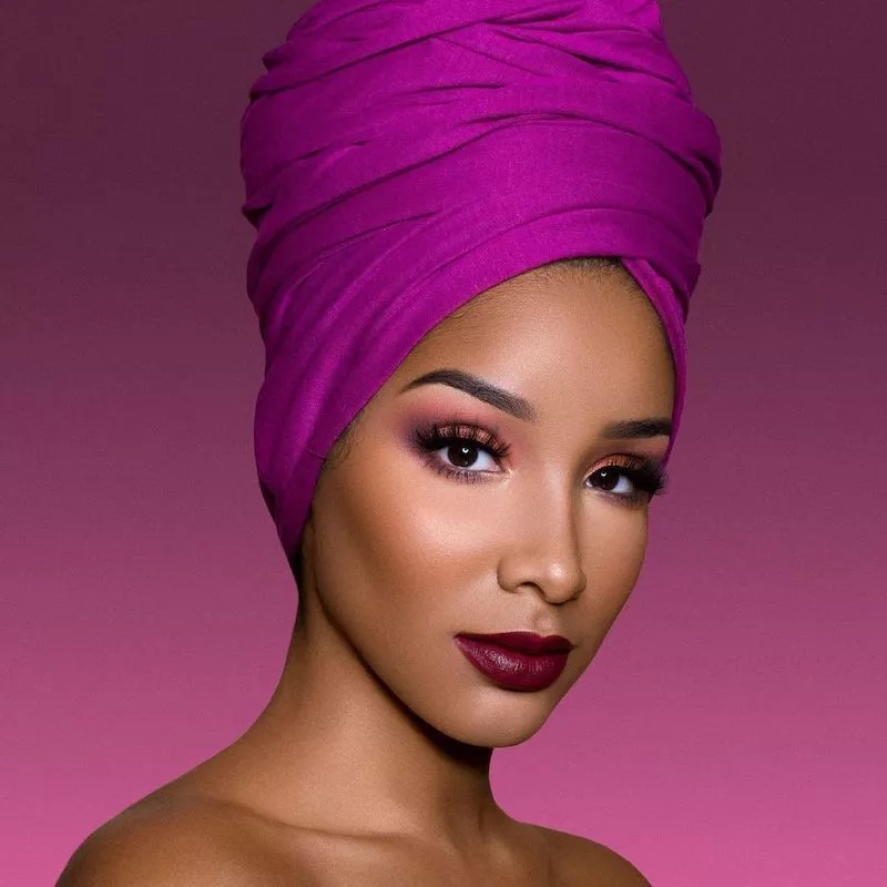 Model wears blended rose-toned eyeshadow, berry lipstick, and pink hair wrap
