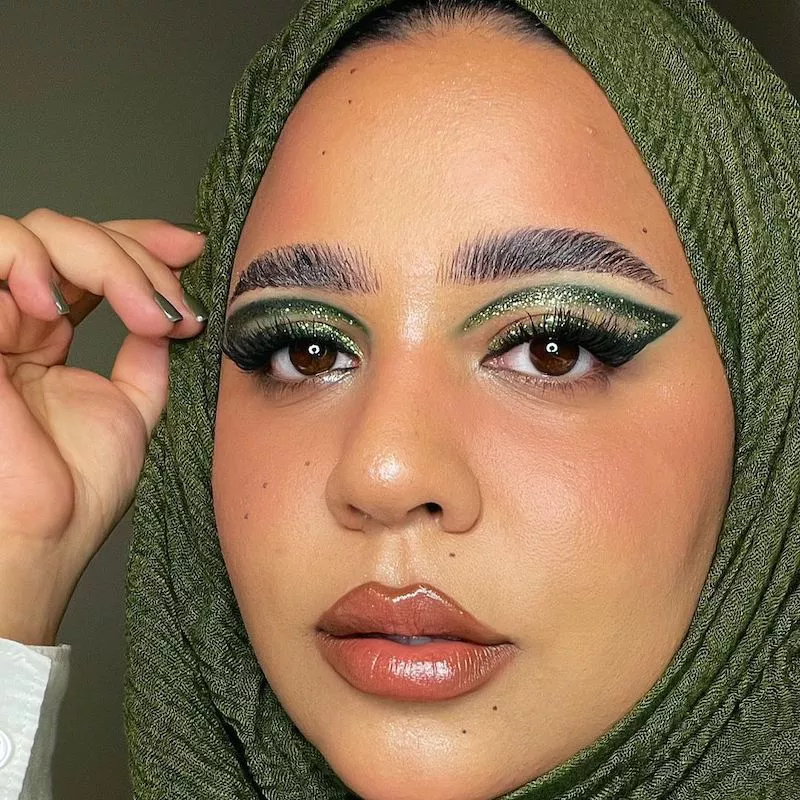 Makeup artist wears green glitter cut crease graphic eyeliner and matching hijab