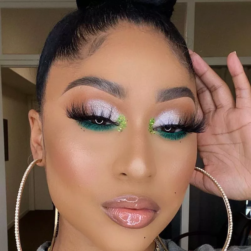 Makeup artist wears silver and green glitter cut crease eye makeup and large hoop earrings