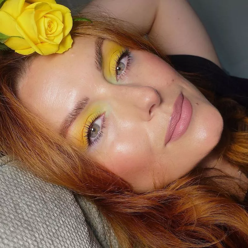 Katie Jane Hughes wears yellow eyeshadow and holds a yellow rose