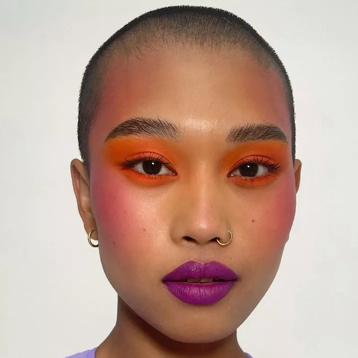 Model with orange eyeshadow, pink blush, and purple lipstick