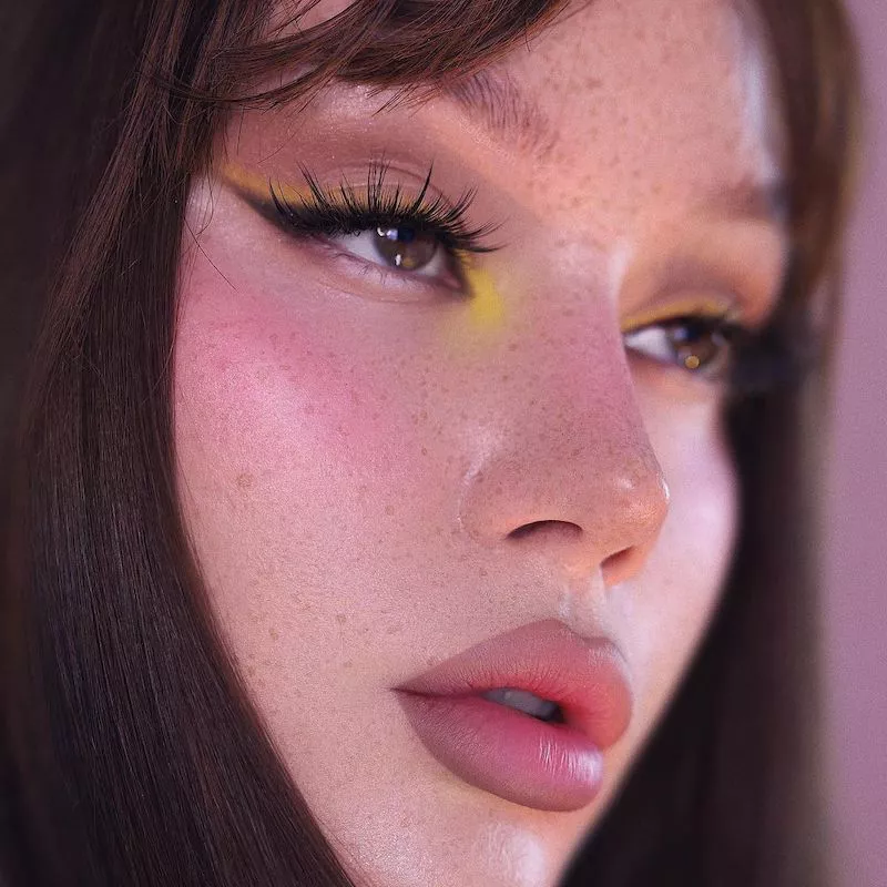 Model wears yellow eyeshadow look with lashes and lined lips