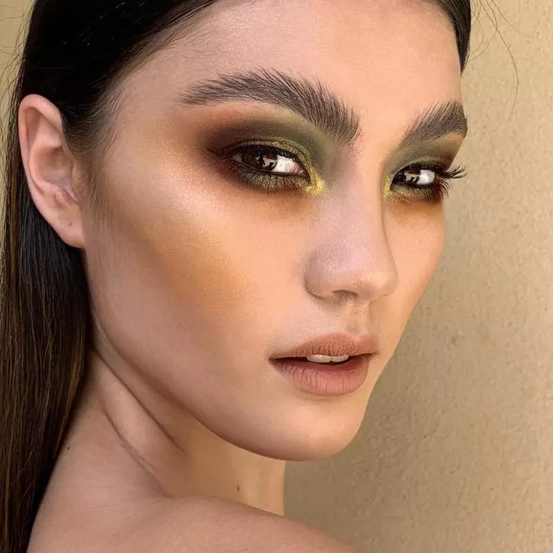 Model with olive, gold, and brown toned smoky eyeshadow and brushed brows