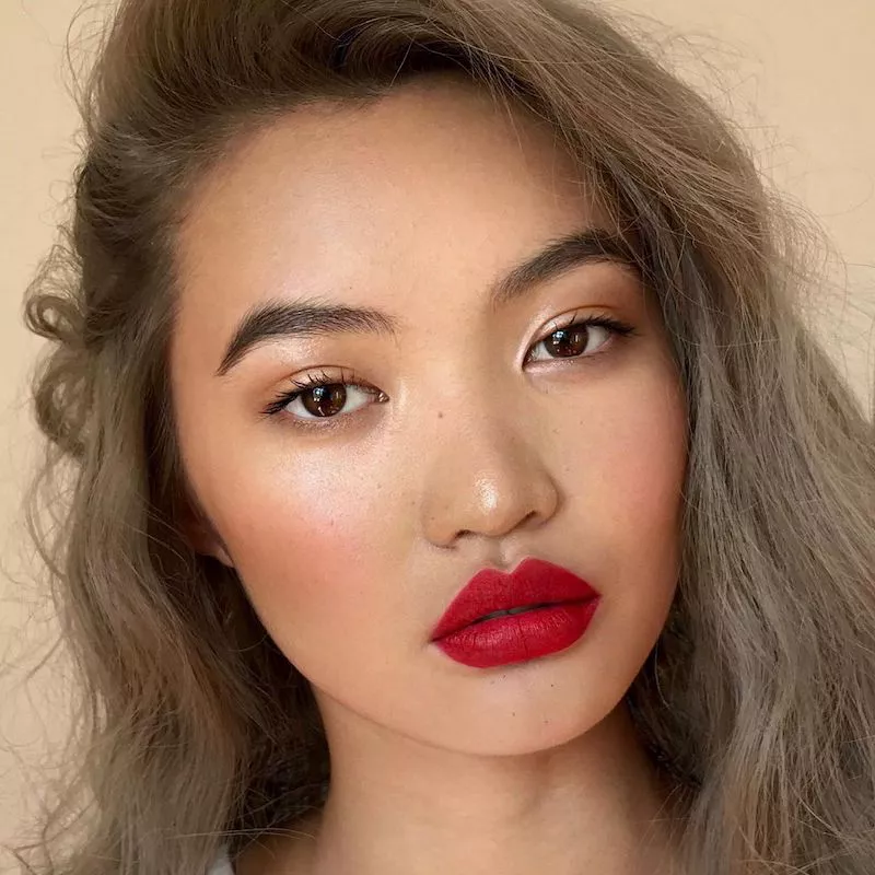 Model wears minimalist shimmery eyeshadow, blush, and bold red lipstick