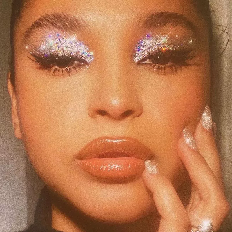 Model wears silver glitter eyelids, winged liner, and nude lipstick