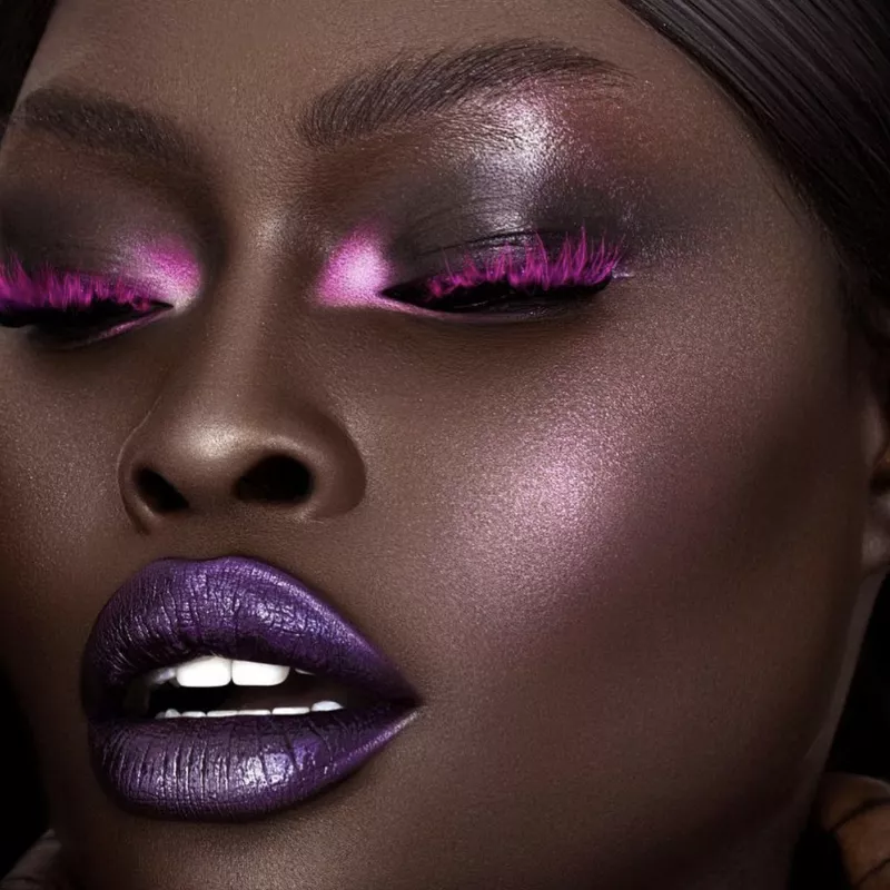 Model with purple glitter lips, pink lashes, and shimmery pink eye and cheek makeup