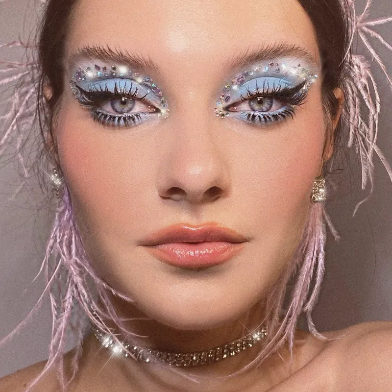 Model wears blue eyeshadow with gem stones and pink feather earrings