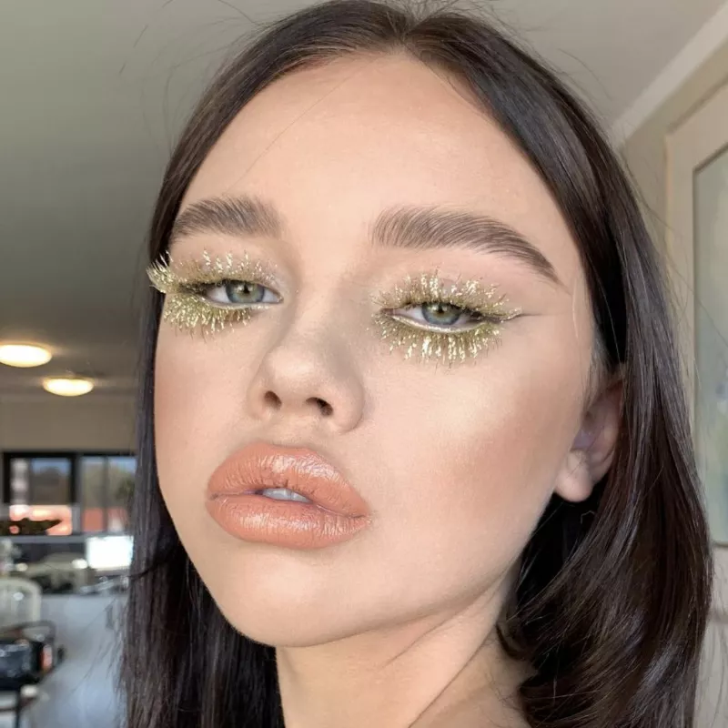 Model with gold false lashes and nude lip