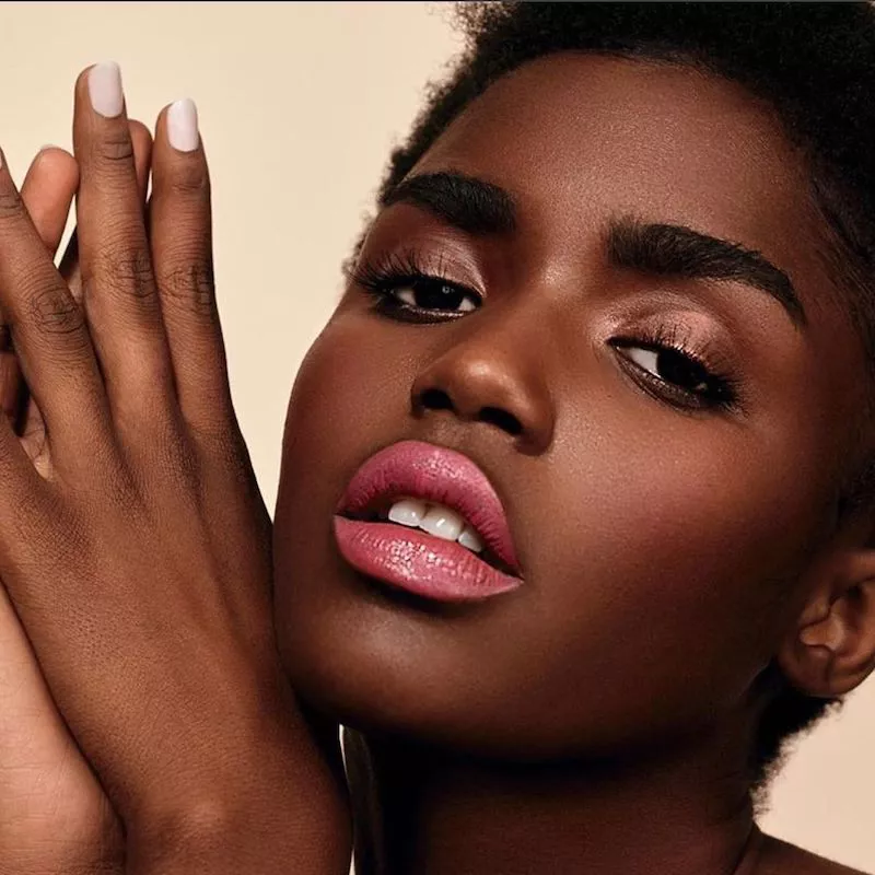 Model with brushed brows, shimmering eyeshadow, pink lipstick, and white manicure