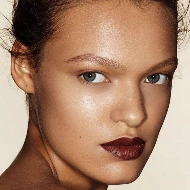 Model with radiant skin and burgundy lipstick